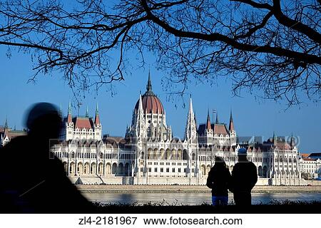 Stock Photo - Silhouette of a couple of people, a man on a bicycle and a tree in front of the Hungarian Parliament Building, a large neo-gothic monument built in the early 20th century, seat of the National Assembly of Hungary. Hungary, Budapest, banks of Danube river.. Fotosearch