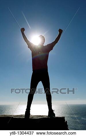 Stock Photo - Silhouette of a male athlete by the sea reaching up to the sky. Fotosearch
