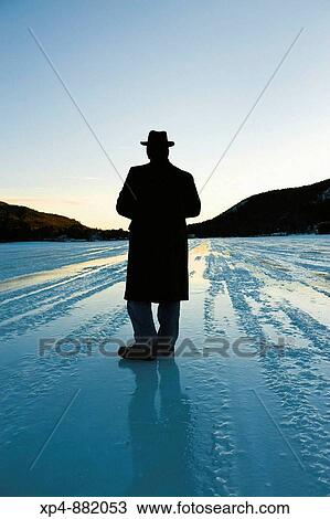 Silhouette of a man wearing an overcoat and a hat standing on a frozen lake strating off to the horizon, his back is to the camera. View Large Photo Image Stock Image - Silhouette of a man wearing an overcoat and a hat standing on a frozen lake strating off to the horizon, his back is to the camera.. Fotosearch
