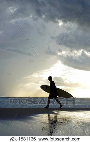 Silhouette of a surfer walking with his surfboard along the beach with stormy clouds in the background, Tarifa, Andalucia, Spain View Large Photo Image Stock Photograph - Silhouette of a surfer walking with his surfboard along the beach with stormy clouds in the background, Tarifa, Andalucia, Spain. Fotosearch