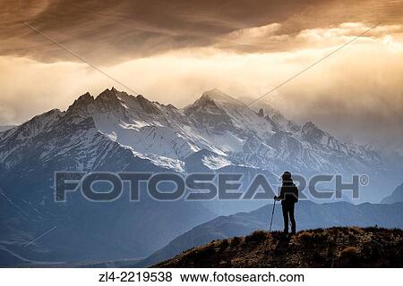 Stock Photo - Silhouette of a trekker watching the mountains in the evening sun light. Nepal, Gandaki, Upper Mustang (near the border with Tibet). Model Released.. Fotosearch