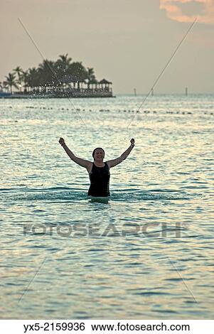 Stock Photograph - Silhouette of a woman bathing on a beach at sunset.. Fotosearch