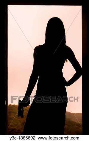 Stock Image - Silhouette of a woman holding a gun while standing in a door frame. Fotosearch