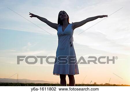 Silhouette of a young woman standing in field at dusk arms raised View Large Photo Image Stock Image - Silhouette of a young woman standing in field at dusk arms raised. Fotosearch