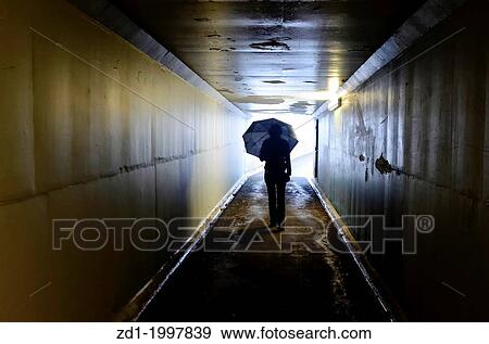 Stock Photo - Silhouette of woman holding an umbrella and walking in a tunnel. Light at End of Tunnel concept.. Fotosearch