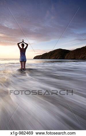 Stock Photo - Silhouette of young woman doing yoga at the beach during sunset in Playas del Coco, Costa Rica. Fotosearch