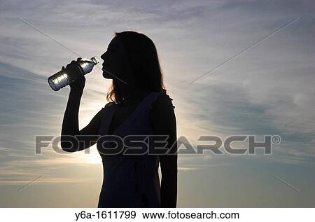 Silhouette of young woman drinking bottle of water View Large Photo Image Stock Photo - Silhouette of young woman drinking bottle of water. Fotosearch