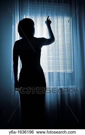 Silhouetted woman standing by window reaching for light View Large Photo Image Stock Photograph - Silhouetted woman standing by window reaching for light. Fotosearch