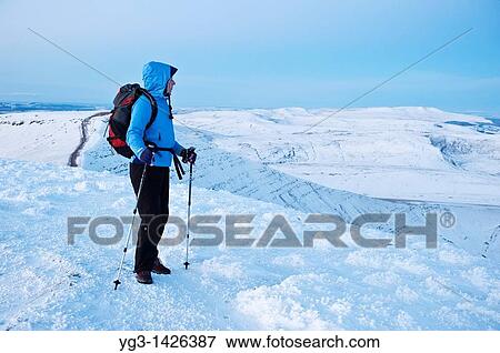 Stock Photo - Single female hiker takes in winter view of Welsh landscape from summit of Pen Y Fan, Brecon Beacons national park, Wales. Fotosearch