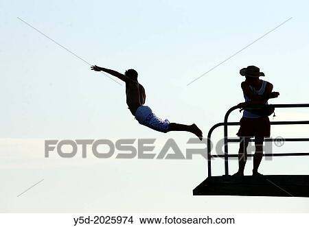 Picture - Single man jumping from diving platform to waters of Geneva Lake, safe guard watching jumping man, Paquis beach, Geneva, Switzerland. Fotosearch