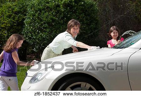 Stock Photo - Single mom and daughters family washing car at home in driveway together with hose and having fun. Fotosearch