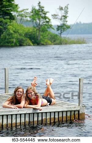 Stock Photography - sisters 13 and 18 yrs laying together on dock. Fotosearch