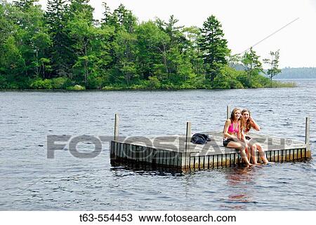 Stock Image - sisters 13 and 18 yrs sitting on dock together at cottage. Fotosearch
