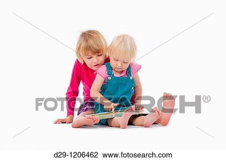 Stock Image - sisters looking at chidren's book - isolated on white. Fotosearch