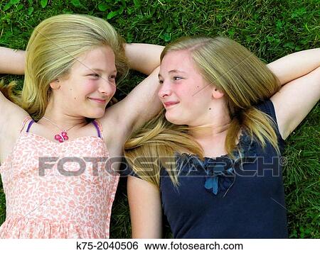 Sisters lying down on lawn looking at each other View Large Photo Image Stock Photograph - Sisters lying down on lawn looking at each other. Fotosearch