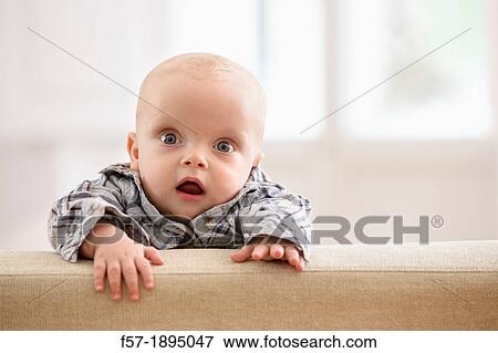 Six month year old baby holding on to the back of a sofa View Large Photo Image Stock Photo - Six month year old baby holding on to the back of a sofa. Fotosearch