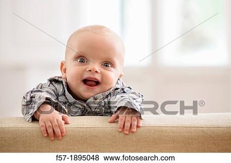 Six month year old baby holding on to the back of a sofa View Large Photo Image Stock Photo - Six month year old baby holding on to the back of a sofa. Fotosearch
