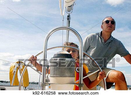 Six year old girl at the helm of a sailboat with her father looking on View Large Photo Image Stock Photo - Six year old girl at the helm of a sailboat with her father looking on. Fotosearch