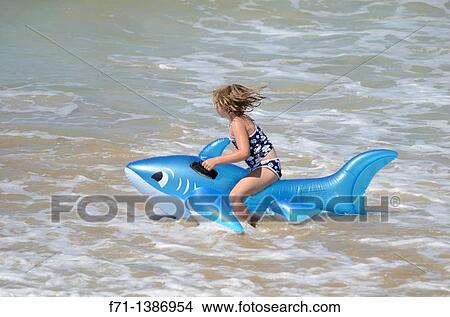 Picture - Six year old girl on the beach playing in the surf on inflatable shark Mimiwhangata Northland, New Zealand. South Pacific Ocean. Fotosearch