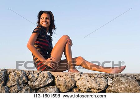 Slender young woman is sitting on the wall edge, watching sunset View Large Photo Image Stock Photo - Slender young woman is sitting on the wall edge, watching sunset. Fotosearch