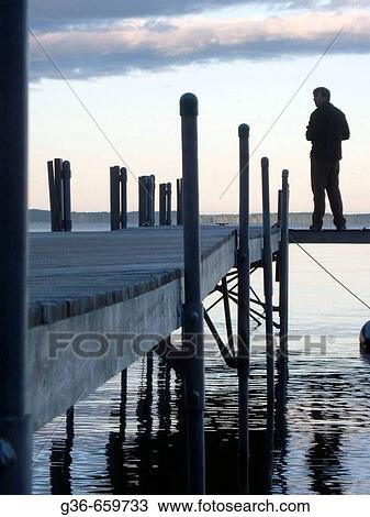 Stock Image - Small dock with people walking on it at sunset in Sebago Lake, Maine. Fotosearch