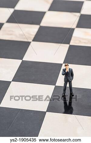Stock Photography - Small figurine of businessman standing on chessboard and thinking of strategic planning. Fotosearch
