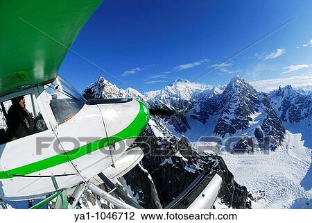 Stock Image - Small float plane Piper PA-20 Pacer flying over Alaska Range mountains and glacier of Denali National Park. In background the highest peak of north america: Mont Mac Kinley. Viewed from the south side. Alaska, USA. Fotosearch