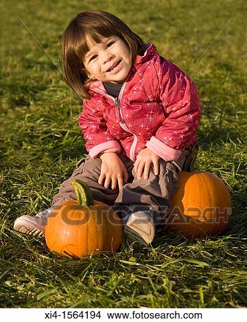 Smiley toddler sat on the green grass with 2 pumpkins View Large Photo Image Picture - Smiley toddler sat on the green grass with 2 pumpkins. Fotosearch