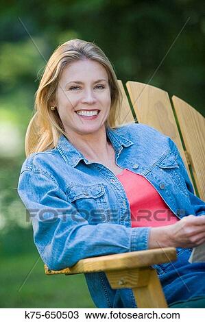 Stock Image - smililng woman sitting in chair outdoors. Fotosearch