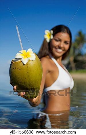 Stock Photo - Smiling, attractive local girl holds out a coconut with straw and flower ready to drink at Lahaina, Maui, Hawaii. Fotosearch