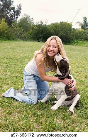 Smiling blonde teen girl in blue jeans and white tank top kneeling on grass lawn, get's a kiss from her pet dog. View Large Photo Image Stock Image - Smiling blonde teen girl in blue jeans and white tank top kneeling on grass lawn, get's a kiss from her pet dog.. Fotosearch