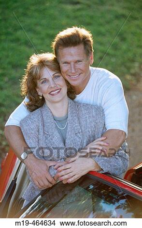 Picture - smiling couple standing by their car. Fotosearch
