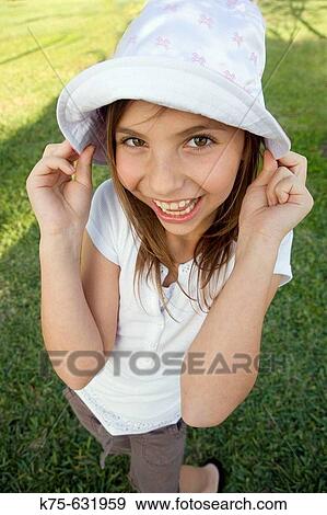 Stock Photo - Smiling girl with hands pulling on her hat.. Fotosearch