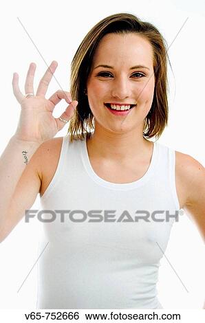 Stock Photograph - smiling happy positive 19 year old teenage girl wearing white vest giving the OK sign with the fingers of her right hand. Fotosearch
