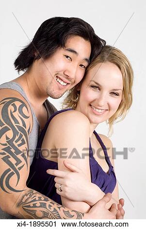 Smiling multicultural couple, asian & caucasian couple hugging Both are looking into the camera, he has a long tatoo in the arm White background View Large Photo Image Stock Image - Smiling multicultural couple, asian & caucasian couple hugging Both are looking into the camera, he has a long tatoo in the arm White background. Fotosearch