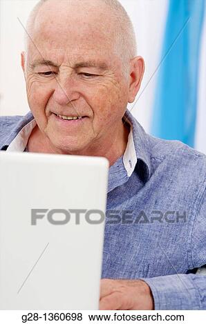 Smiling Senior man using his computer at home View Large Photo Image Stock Photo - Smiling Senior man using his computer at home. Fotosearch