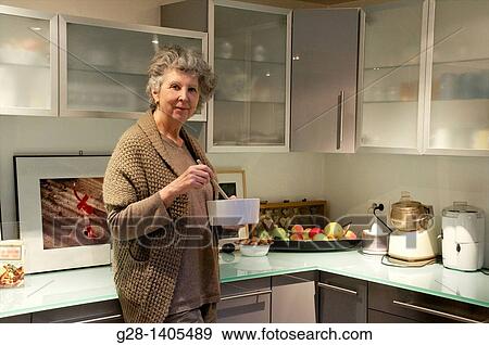 Stock Photo - Smiling senior woman holding a dish and preparing a meal in her kitchen. Fotosearch