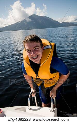 Stock Photo - Smiling teenage boy with dental braces climbs on board boat after water ski biscuit ride - Lake Brunner, South Island of New Zealand. Fotosearch