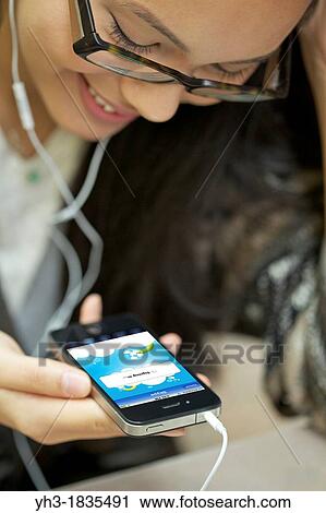 Smiling young female wearing headphone making phone call using Skype with iphone 4 View Large Photo Image Stock Image - Smiling young female wearing headphone making phone call using Skype with iphone 4. Fotosearch