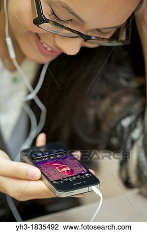 Smiling young female wearing headphone listening music using her iphone 4 View Large Photo Image Stock Image - Smiling young female wearing headphone listening music using her iphone 4. Fotosearch
