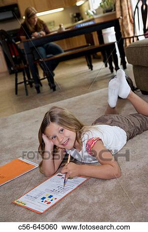 smiling young girl does her homework on floor, mother in background. View Large Photo Image Stock Image - smiling young girl does her homework on floor, mother in background.. Fotosearch