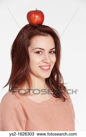 Stock Image - Smiling young woman balancing apple on her head. Fotosearch