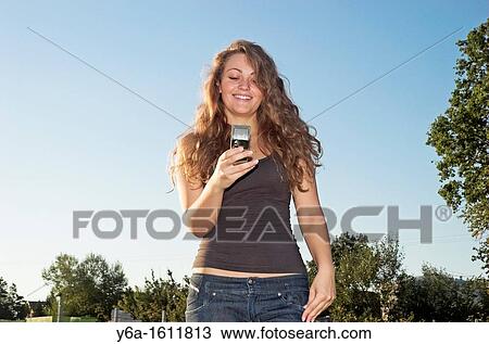 Smiling young woman in park using cell phone View Large Photo Image Stock Image - Smiling young woman in park using cell phone. Fotosearch
