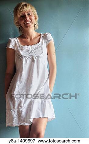 Stock Photo - Smiling young woman in romantic white dress leaning against blue wall. Fotosearch