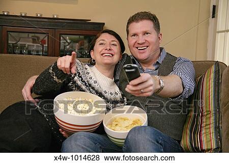 Snacking while lounging on the sofa at home is a fun pastime of otherwise busy couples Pictured here is a couple snacking on popcorn and potato chips while watching TV and relaxing together on their living room couch View Large Photo Image Stock Photo - Snacking while lounging on the sofa at home is a fun pastime of otherwise busy couples Pictured here is a couple snacking on popcorn and potato chips while watching TV and relaxing together on their living room couch. Fotosearch