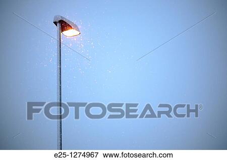 Snow falls past an illuminated street lamp in winter View Large Photo Image Stock Photo - Snow falls past an illuminated street lamp in winter. Fotosearch