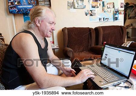 Picture - Sofia, Bulgaria. A middle aged Bulgarian man with his laptop in his living room.. Fotosearch
