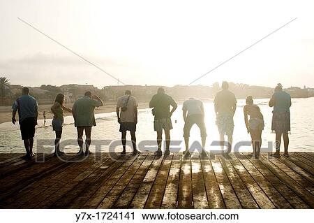 Stock Image - Some tourists watching a fisherman working below the dock in Santa Mar? a, Sal island, Cape Verde archipelago, Africa. Fotosearch
