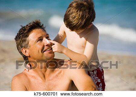 Stock Image - Son putting sunscreen on dad's nose. Fotosearch