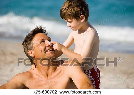 Stock Image - Son putting sunscreen on dad's nose. Fotosearch